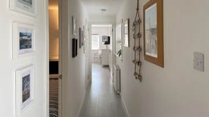 A hallway with framed pictures on the walls, a radiator, and a white door leading to another room. - A beautiful coastal cottage in characterful Portmahomack. (Portmahomack, near Dornoch)