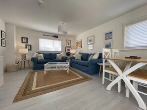A modern living room with a blue sofa set, a white coffee table, and a dining table with chairs.
