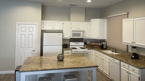 A modern kitchen with white cabinets, granite countertops, a refrigerator, stove, microwave, and a sign that says "GATHER". - Desert Oasis salt water Pool/spaHome, Gated Community w/LAKE (Indio)