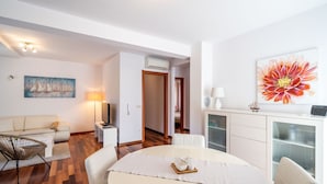 A modern living room with a sofa, coffee table, and dining table set up. There is a painting on the wall and a large flower artwork above the dining table. - Lorena Suite - Two Bedroom Apartment with Private Pool (Dubrovnik)