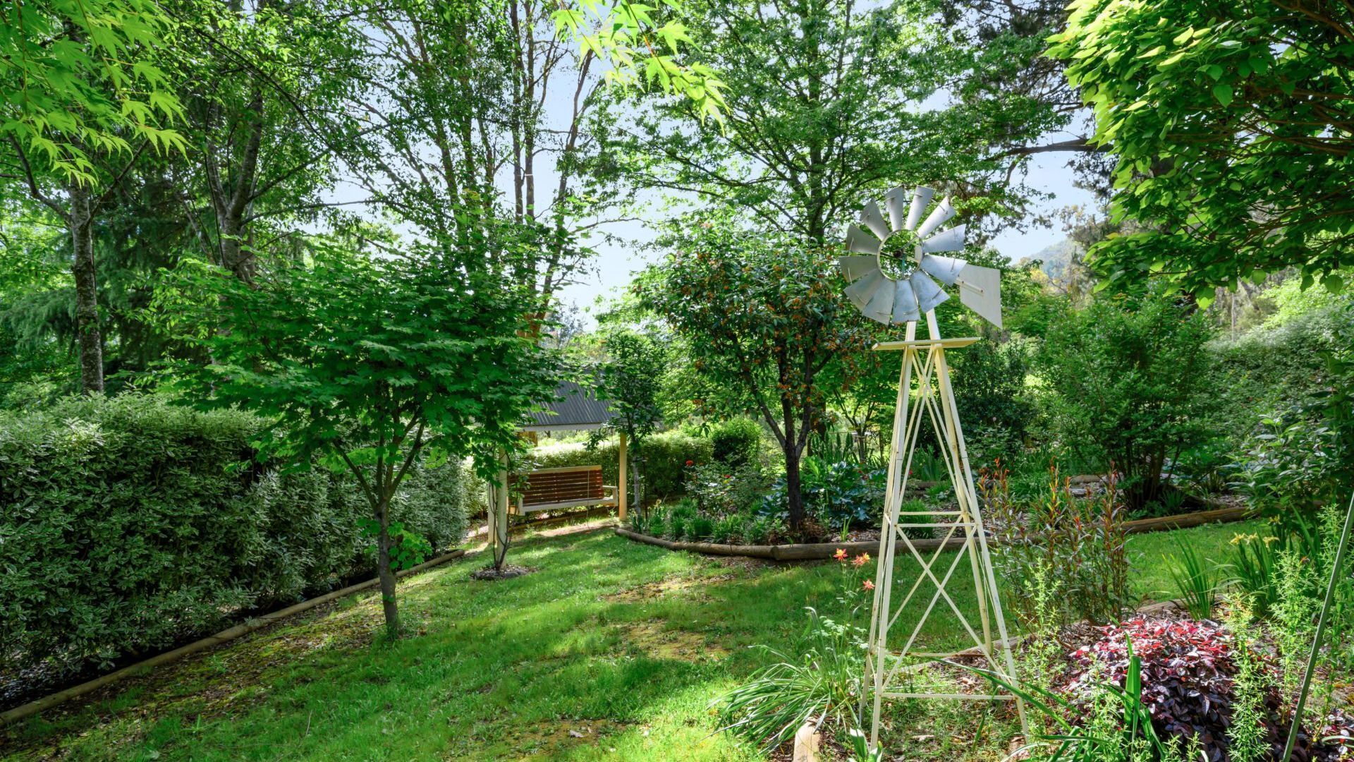 A lush garden with a windmill, a wooden bench, and a variety of plants.