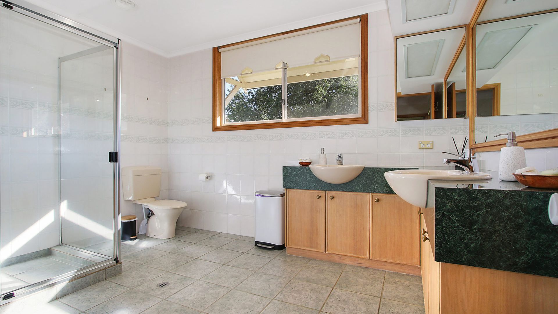 Une salle de bain moderne avec une douche à parois de verre, des toilettes, un lavabo avec un plan de travail en marbre, des meubles en bois et un grand miroir.