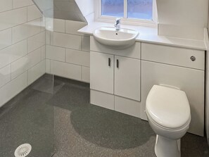 A bathroom with white tiles, a sink, cabinets, and a toilet. - Stepping Stone Cottage (Bacton, near North Walsham)