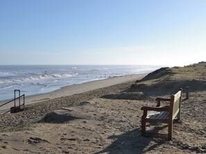 A beach with a wooden bench and a lifeguard tower. - Stepping Stone Cottage (Bacton, near North Walsham)