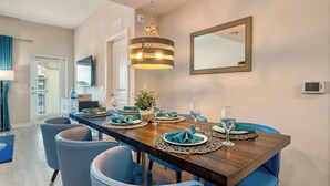 A dining area with a long wooden table, blue chairs, and a hanging light fixture. - VCR4-410- 3BR Condo with Resort Access Near Disney (Orlando)