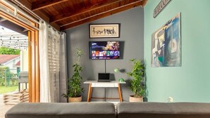 Ett rum med ett skrivbord, två krukväxter, en tv och en soffa.