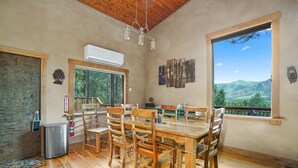 A dining area with a wooden table and chairs, a view of mountains through a large window, and an air conditioning unit on the wall. - Beautiful Rustic Mountain Home (Durango)