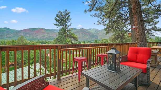 A deck with a wooden railing, red seating, and a table with a lantern. - Beautiful Rustic Mountain Home (Durango)