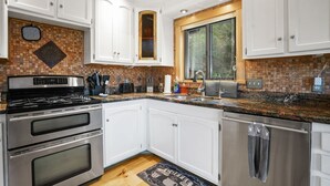 A modern kitchen with white cabinets, a double oven, a stainless steel refrigerator, and a window with a view of greenery. - Beautiful Rustic Mountain Home (Durango)