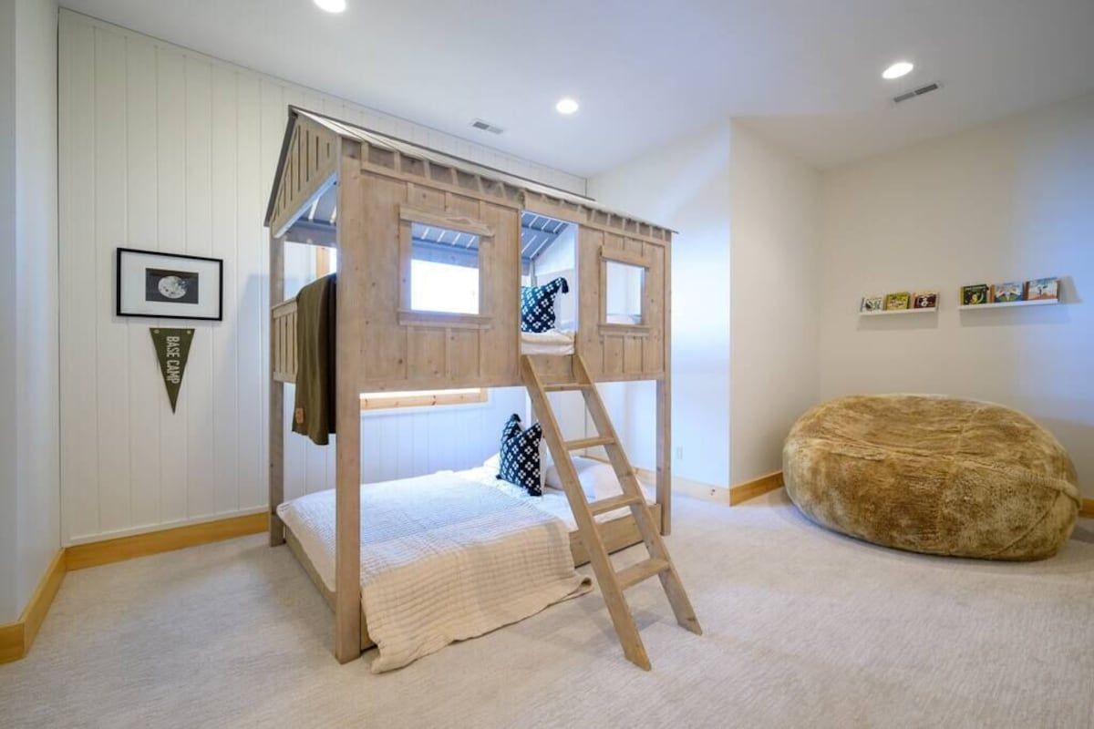 A bunk bed with a ladder, a soft round ottoman, and a framed picture on the wall.