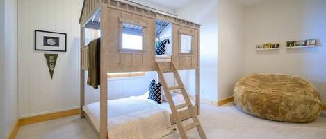 A bunk bed with a ladder, a soft round ottoman, and a framed picture on the wall.