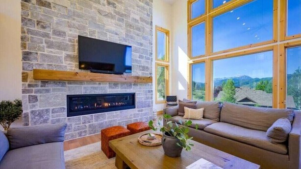 A living room with a stone fireplace, a flat-screen TV, and a large window offering a mountain view. - The Ledges | Ski Getaway | Hot Tub & Theater Room (Eden)