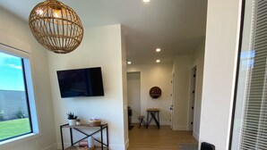 A modern living room with a flat-screen TV, a wicker pendant light, and a wooden floor.