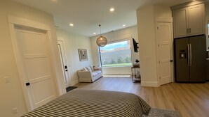 A modern bedroom with a large bed, a view to the outside, and a kitchen area.