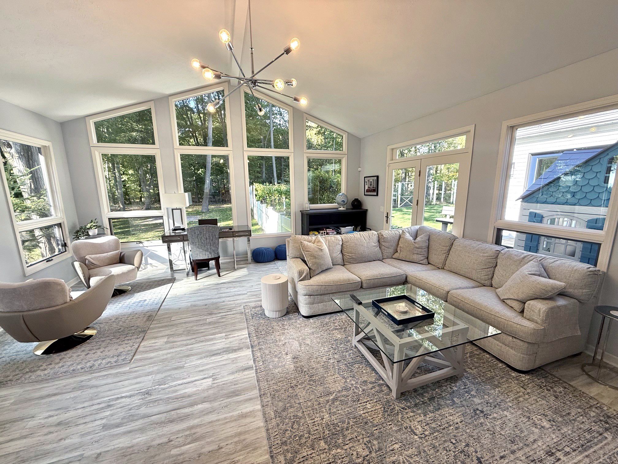 A spacious living room with a large sectional sofa, a glass coffee table, and a modern chandelier.