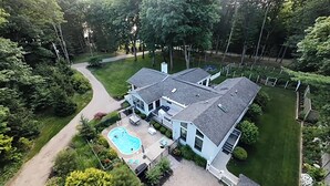A two-story house with a swimming pool, surrounded by a well-maintained lawn and trees. - Ultimate Family Retreat: Pool, Huge Yard, Gardens, Chickens, 5 Beaches Closeby (Fennville)