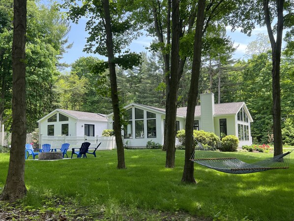 Une maison à l’extérieur blanc, avec un porche et un hamac dans le jardin.