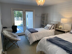 Une chambre avec deux lits, un bureau, une chaise, une échelle et une porte donnant sur un espace extérieur.