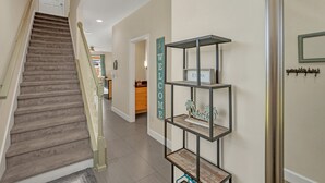 A staircase leading to a landing with a 'WELCOME' sign, a metal shelf unit, and a door with a coat rack. - Cutest Vacation Home Ever! (Clermont)