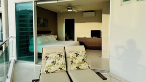Ein Hotelzimmer mit Bett, Schreibtisch, Fernseher und einem Balkon mit Liegestühlen.
