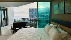 Ein modernes Hotelzimmer mit einem großen Bett, einem Balkon mit Sitzgelegenheit und Blick auf Stadt und Meer.