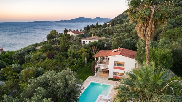 A coastal villa with a swimming pool, surrounded by lush greenery and overlooking the sea.