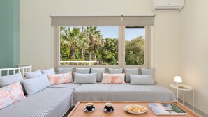 A cozy bedroom with a large window, a bed with striped bedding, a bedside table with a lamp, and a tray with coffee cups and pastries.