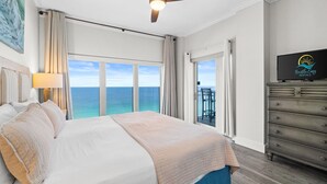 A hotel room with a bed, a ceiling fan, a TV, and a view of the ocean.