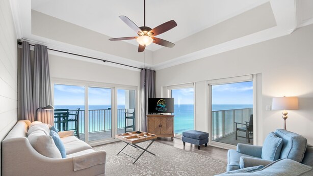 A spacious living room with a balcony, a ceiling fan, a flat-screen TV, and a wooden cabinet.