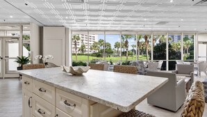 A modern kitchen with a large island, white cabinetry, and a view of palm trees and buildings.