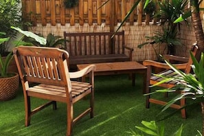 A wooden bench and chairs on a green artificial turf, with a bamboo fence in the background.