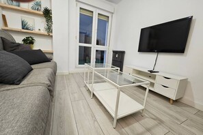 Un salon moderne avec un canapé, une table basse en verre, un meuble TV blanc et un radiateur.