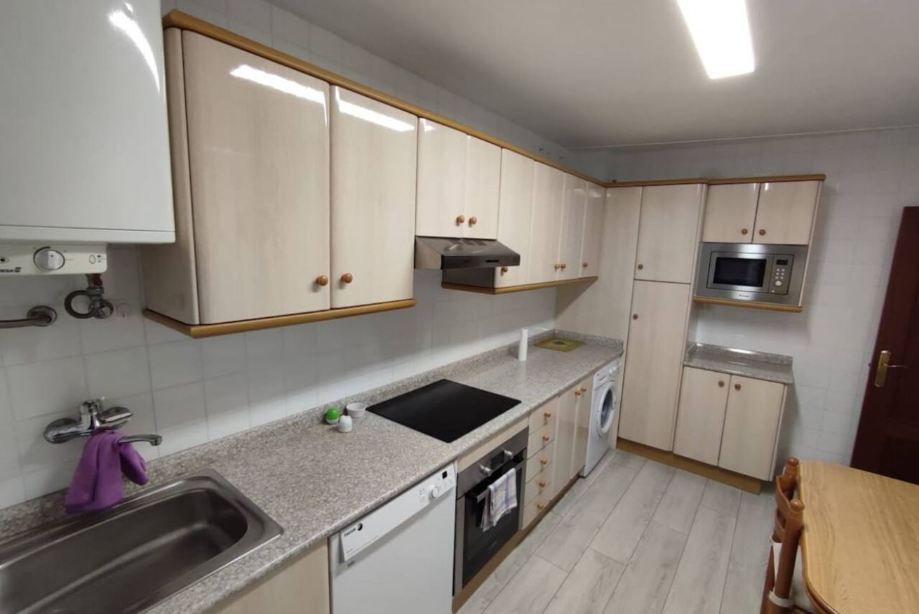Een keuken met witte kastjes, een roestvrijstalen spoelbak, een magnetron en een vaatwasser.
