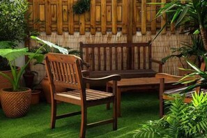 Un conjunto de banco y silla de madera sobre una superficie verde, rodeado de plantas en macetas.