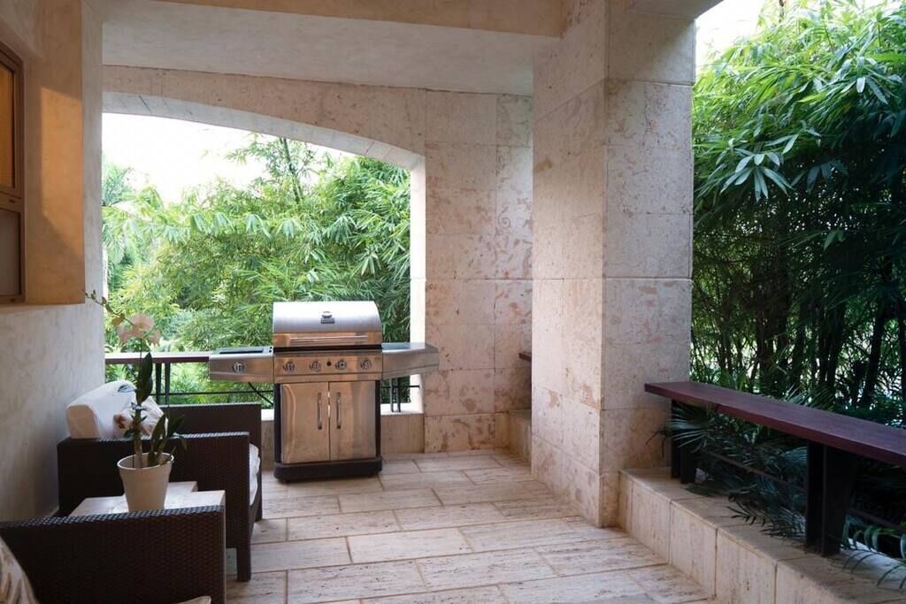 Une terrasse extérieure avec un barbecue, des meubles en osier et une vue sur une végétation luxuriante.
