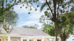 A modern building with a covered outdoor area, a paved walkway, and lush greenery. - Chic luxury condo at Los Altos Casa de Campo (La Romana)