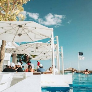 Un espace aménagé au bord de la piscine, avec des parasols, des chaises longues et une vue dégagée sur la mer.