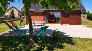 A wooden cabin with a gravel patio, a bench, and two green folding chairs. - Homerez - Chalet in Darazac (Darazac)