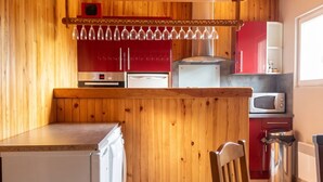 A compact kitchen with wooden walls, a refrigerator, a microwave, and a sink. - Homerez - Chalet in Darazac (Darazac)