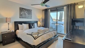 A modern hotel room with a large bed, a ceiling fan, a TV, and a view of the outdoors. - SunBear- AC, Pool, Game Room, Fireplace, Hiking! (Killington)