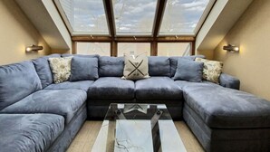 A modern living room with a sectional sofa, a glass coffee table, and a skylight above. - SunBear- AC, Pool, Game Room, Fireplace, Hiking! (Killington)