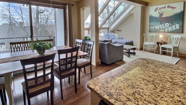 A spacious living area with a dining table, chairs, a sofa, and a large window. - SunBear- AC, Pool, Game Room, Fireplace, Hiking! (Killington)