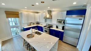 A modern kitchen with white marble countertops, blue cabinets, stainless steel appliances, and a central island with stools.
