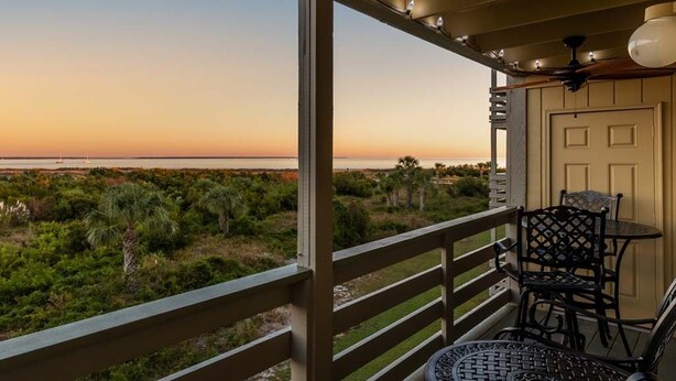 A balcony with a view of the ocean, a door, and a table with chairs. - Lighthouse Point 13B | Oceanfront Condo, Pool! (Tybee Island)