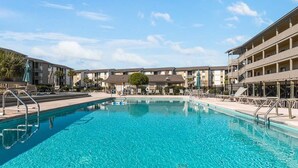 A swimming pool surrounded by multi-story buildings with balconies and outdoor seating areas. - Lighthouse Point 13B | Oceanfront Condo, Pool! (Tybee Island)