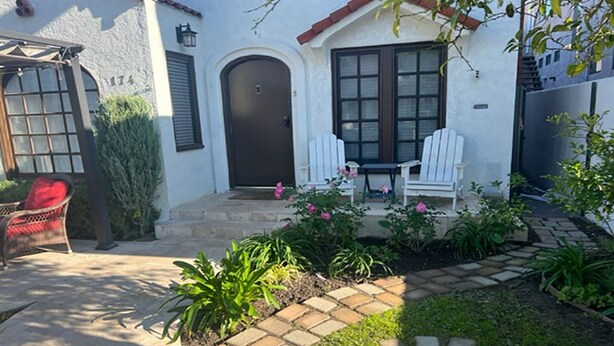A house with a white exterior, a dark brown door, and a small patio area with a white chair and a table. - The Heart of Belmont Shore (Long Beach)