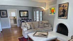A living room with a sofa, ottoman, fireplace, and artwork. - The Heart of Belmont Shore (Long Beach)