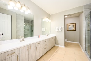 A modern bathroom with a large mirror, dual sinks, and a shower area. - Vista Cay Resort Direct Condos by Millennium Management (Orlando)
