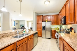 A kitchen with granite countertops, stainless steel appliances, wooden cabinets, and pendant lighting. - Vista Cay Resort Direct Condos by Millennium Management (Orlando)