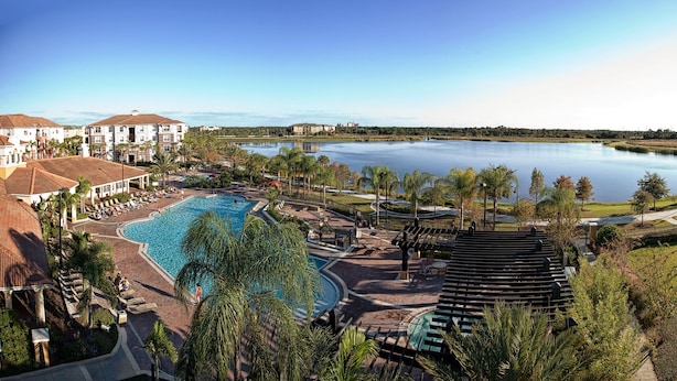 Een resort met een groot zwembad, een tennisbaan en uitzicht op een meer.